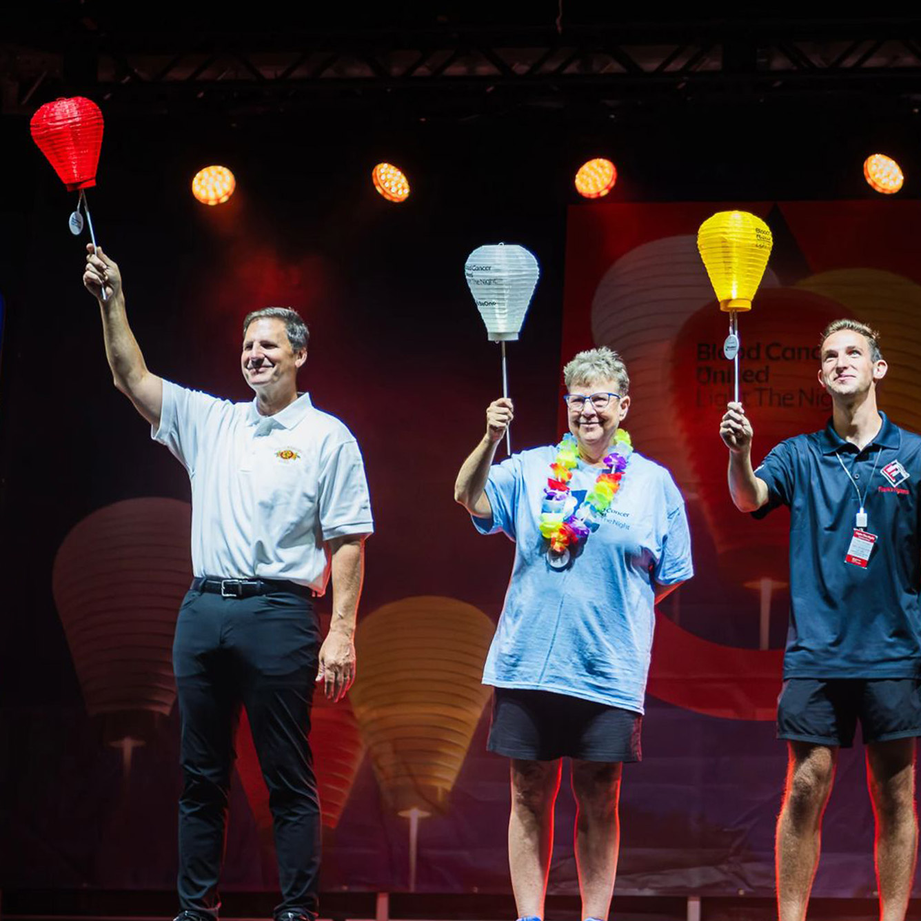 Participants at a Light The Night event holding up red, yellow and white lanterns